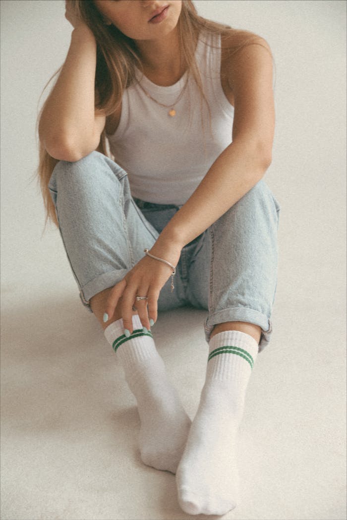 Woman in jeans and socks sitting on a floor in a relaxed pose.