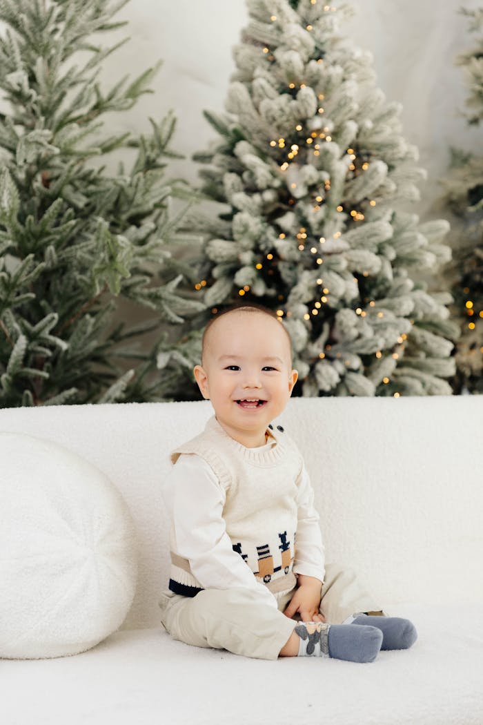 Cheerful baby sitting in a cozy winter-themed setting with Christmas trees.