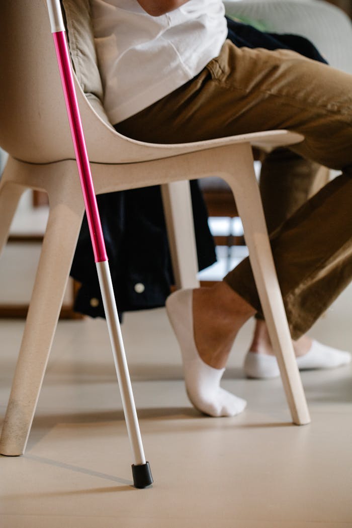 A seated individual rests indoors using a walking stick.