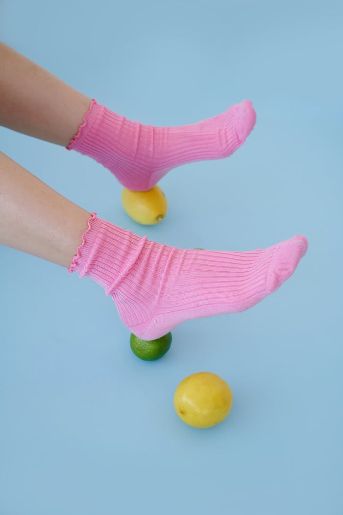 Artistic photo of feet in pink socks balancing on lemons and limes on a blue background.